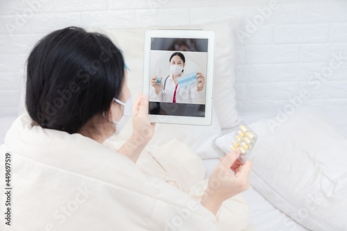 Fototapeta Naklejka Na Ścianę i Meble -  Woman patient examines body temperature during consultation with smart doctor. Sick woman in bed video call to doctor using tablet. Concept of home isolation telemedicine and patient counseling online