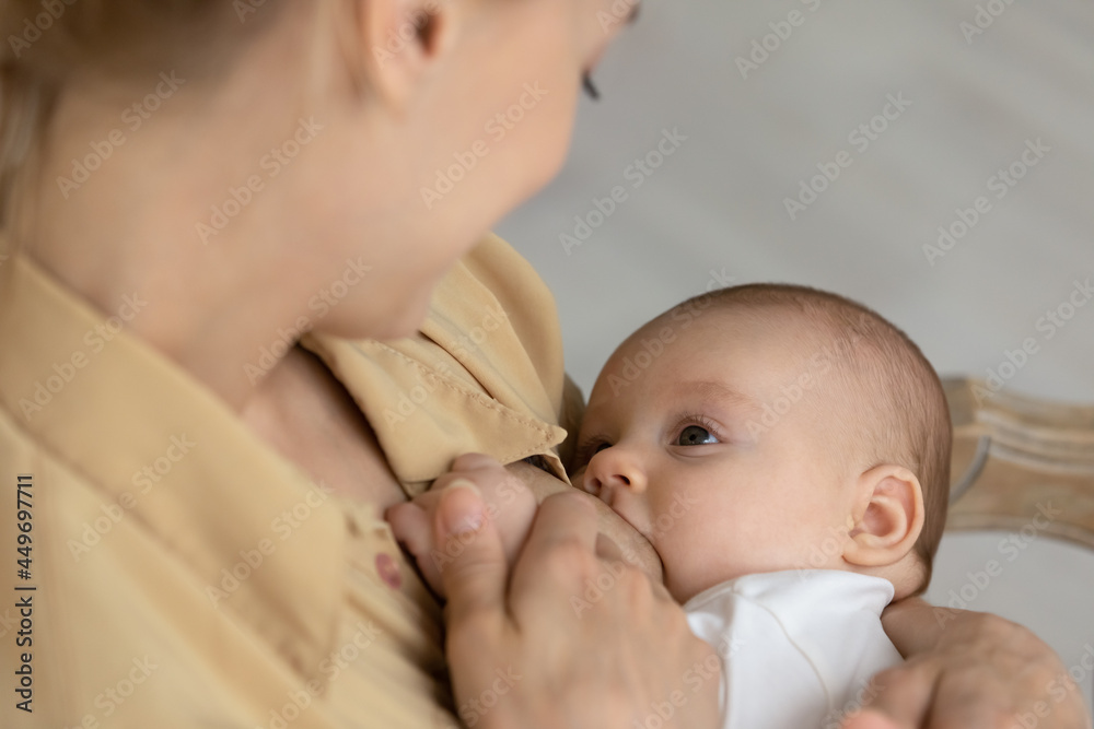 Close up of young mother hold small newborn child in arms breastfeed kid at home. Happy mom sit in chair feed with breast milk little baby infant son or daughter. Motherhood, parenthood concept. Close up of young mother hold small newborn child in arms breastfeed kid at home. Happy mom sit in chair feed with breast milk little baby infant son or daughter. Motherhood, parenthood concept.