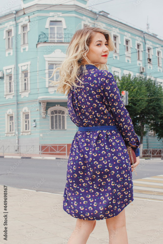Naklejka premium Young beautiful woman in blue dress with a round bag walking on the spring street. Urban background. Stylish Tourist girl enjoying walking the city during weekend trip.