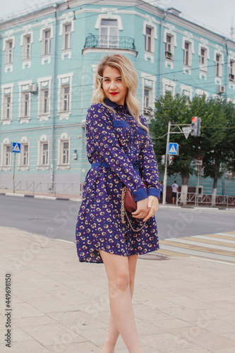 Young beautiful woman in blue dress with a round bag walking on the spring street. Urban background. Stylish Tourist girl enjoying walking the city during weekend trip. © Air_Lady
