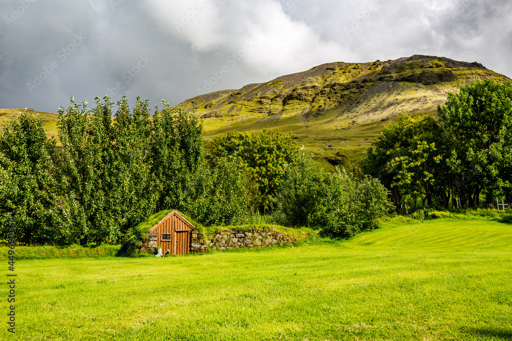 Fresh summer green view from Southern Iceland. Small stone service house covered in moss and grass next to small forest and hill Fresh summer green view from Southern Iceland. Small stone service house covered in moss and grass next to small forest and hill