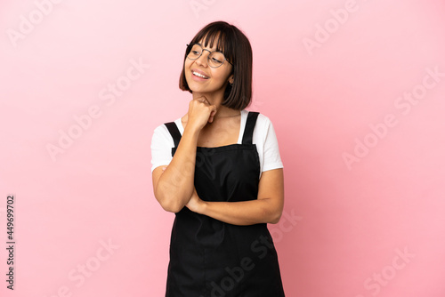 Restaurant waiter over isolated pink background looking up while smiling