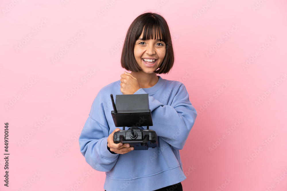 Young mixed race woman holding a drone remote control isolated on pink background celebrating a victory Young mixed race woman holding a drone remote control isolated on pink background celebrating a victory