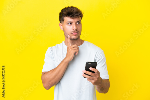 Young caucasian handsome man isolated on yellow background using mobile phone and thinking