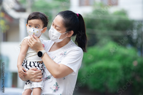 Asian mother wearing white face mask holding her little toddler baby girl who is her daughter, she try to take care her baby by wearing face mask to baby, COVID-19 concept