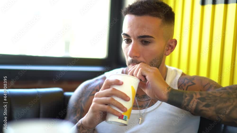 Chico joven tatuado en restaurante tomando un refresco