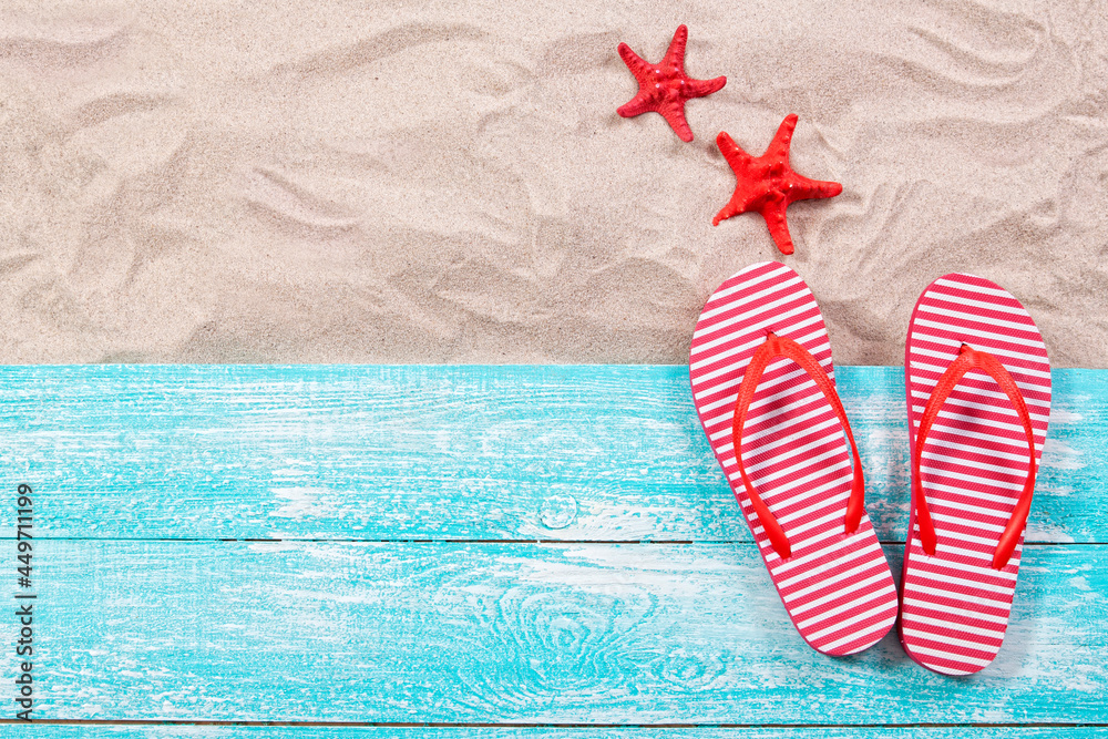 Fototapeta premium Red starfish and flip flops on the sand and wooden board top view