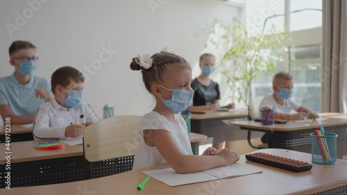 Wallpaper Mural children at school sit in the classroom and raise their hands answering the teacher's questions in protective masks in slow motion Torontodigital.ca