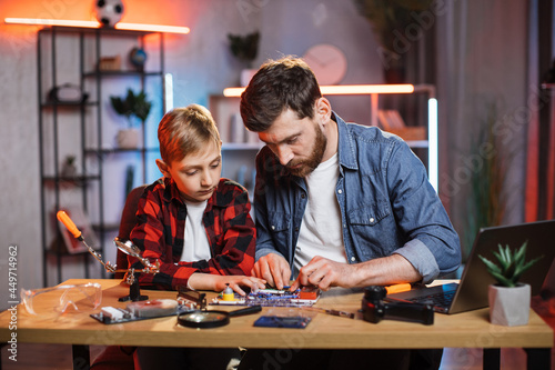 Handsome bearded man and little boy using child designer for making simple electric circuit. Young father teaching his son doing physics experiment at home.