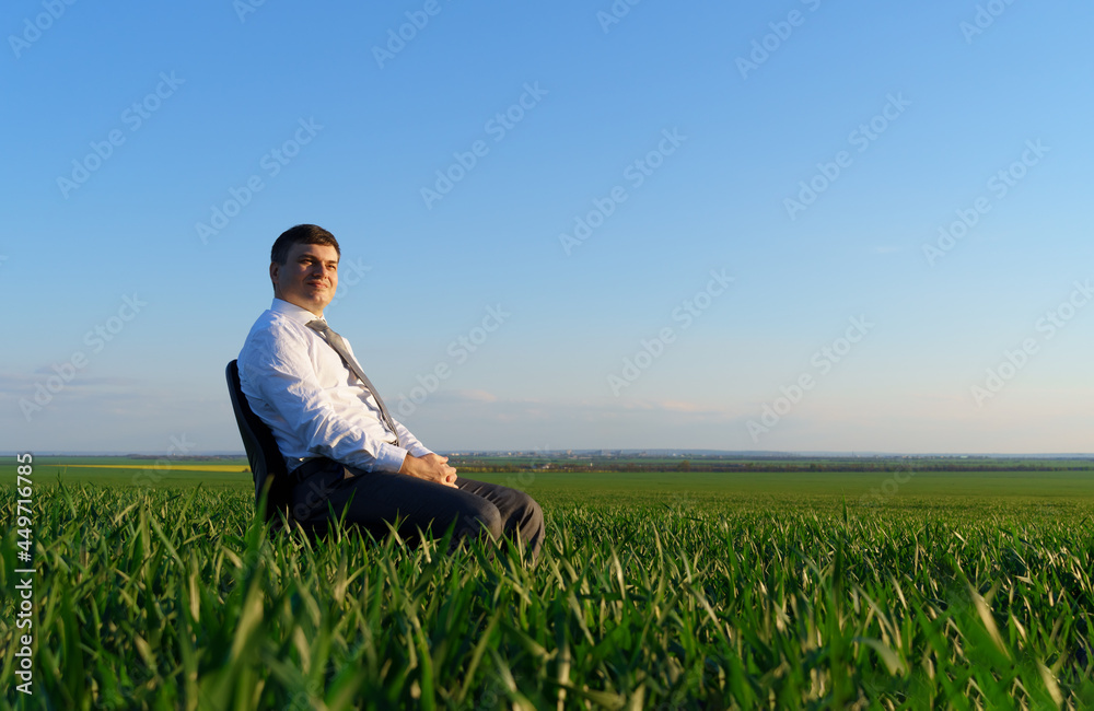 businessman sits in an office chair in a field and rests, freelance and business concept, green grass and blue sky as background businessman sits in an office chair in a field and rests, freelance and business concept, green grass and blue sky as background