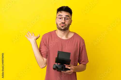 Man holding a drone remote control isolated on yellow background having doubts while raising hands