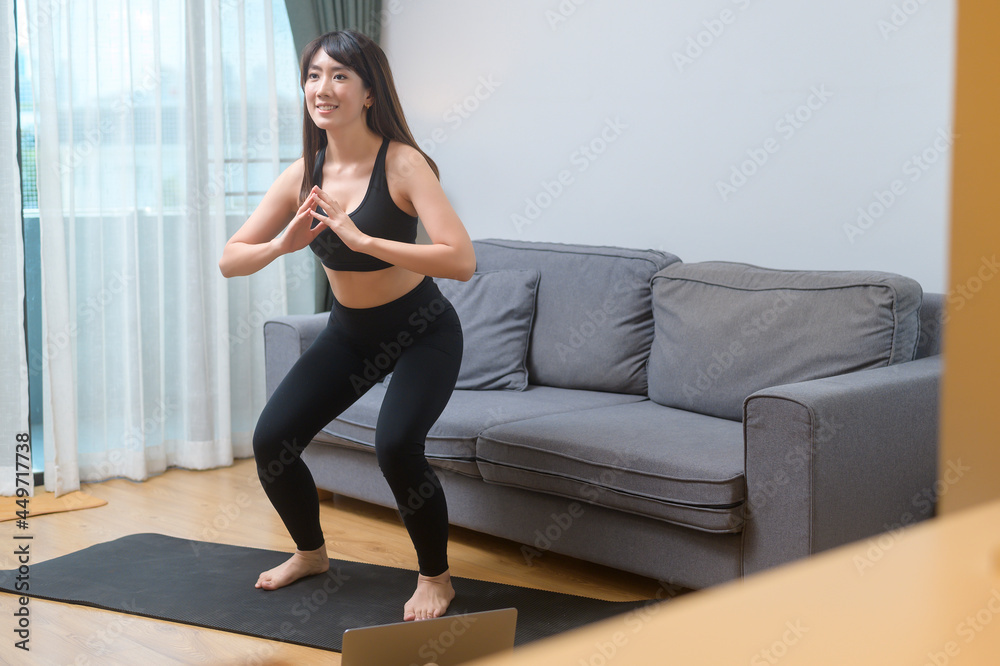 Young woman is exercising and watching online training fitness class on the laptop in living room at home, sport, fitness and technology concept. Young woman is exercising and watching online training fitness class on the laptop in living room at home, sport, fitness and technology concept.