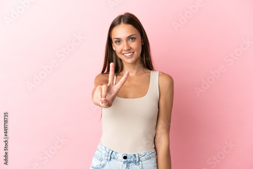 Young woman over isolated pink background smiling and showing victory sign