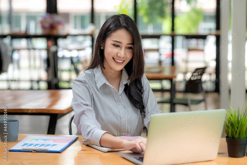 Front view of attractive young Asian business woman sitting using laptop graph placed at the office. Front view of attractive young Asian business woman sitting using laptop graph placed at the office.