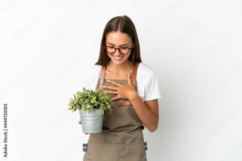 Gardener girl holding a plant over isolated white background smiling a lot Gardener girl holding a plant over isolated white background smiling a lot