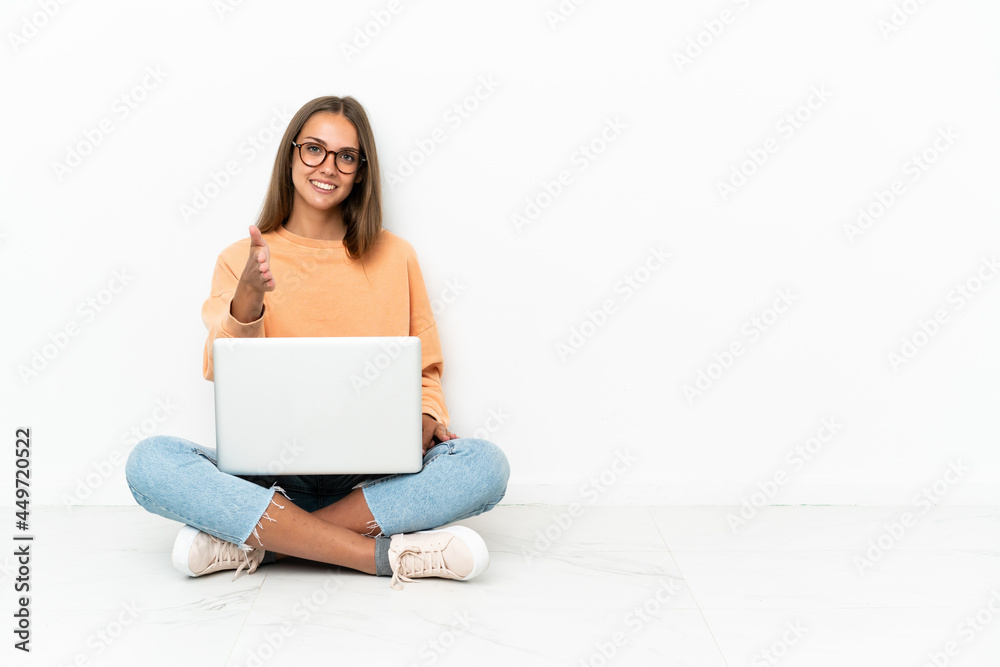 Young woman with a laptop sitting on the floor shaking hands for closing a good deal