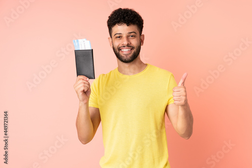 Young Moroccan man isolated on pink background in vacation holding a passport and plane with thumb up