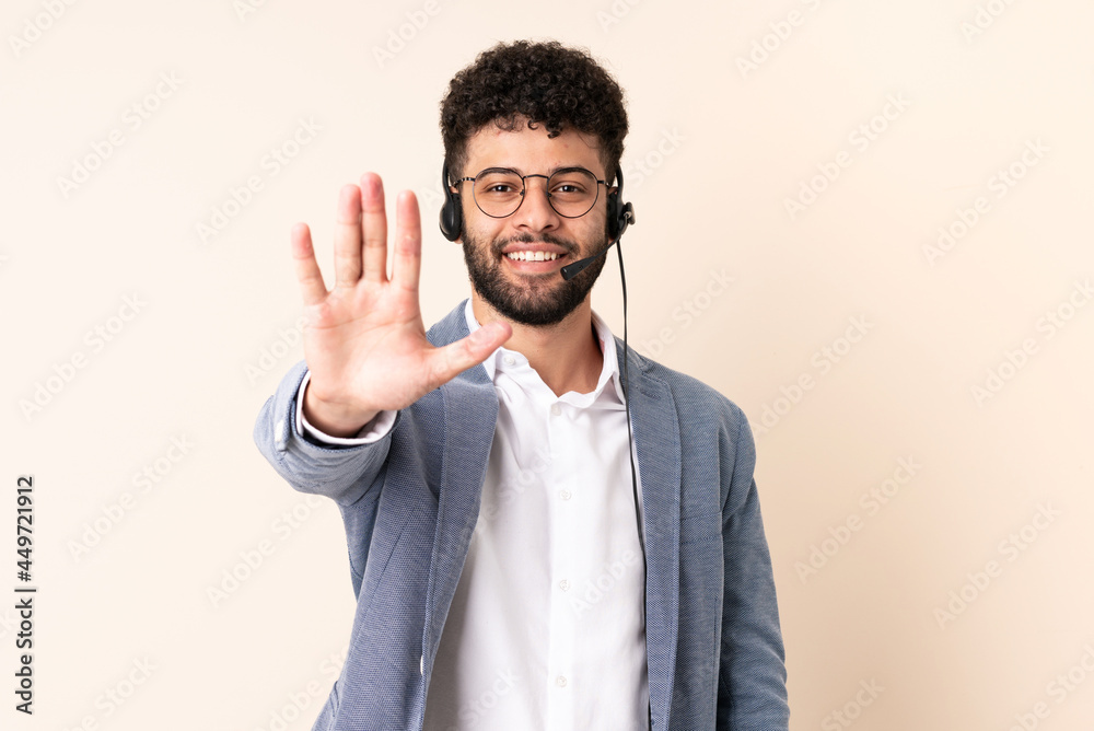 Telemarketer Moroccan man working with a headset isolated on beige background making stop gesture