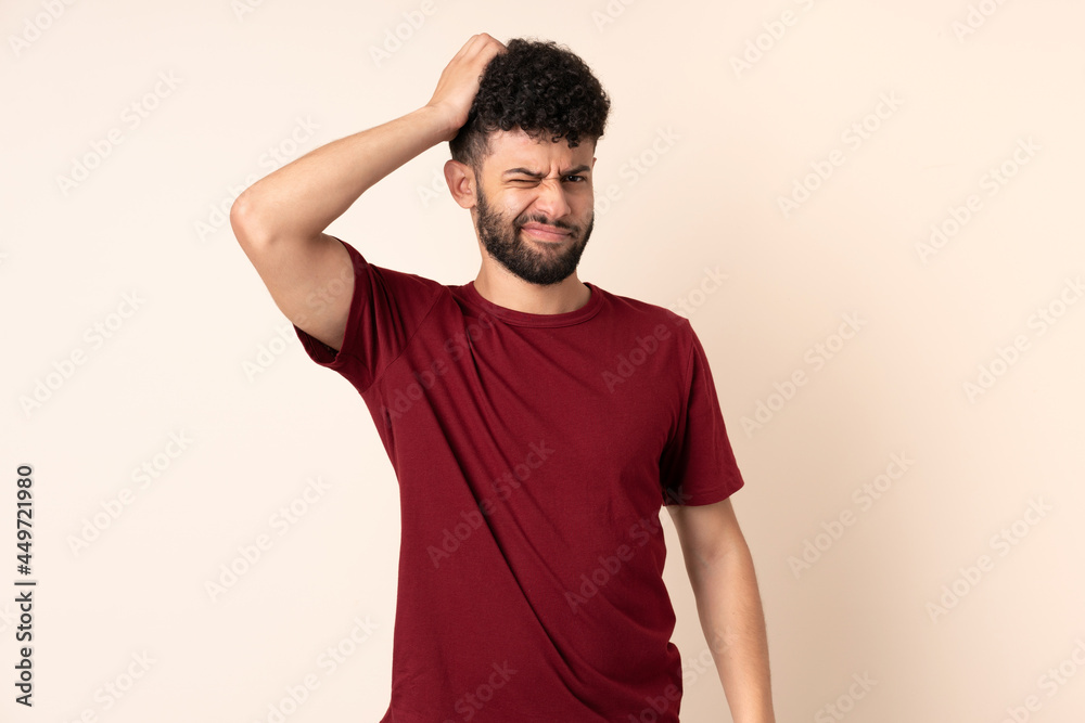 Young Moroccan man isolated on beige background having doubts while scratching head Young Moroccan man isolated on beige background having doubts while scratching head