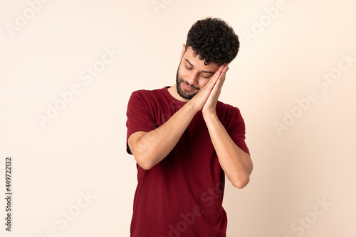 Young Moroccan man isolated on beige background making sleep gesture in dorable expression