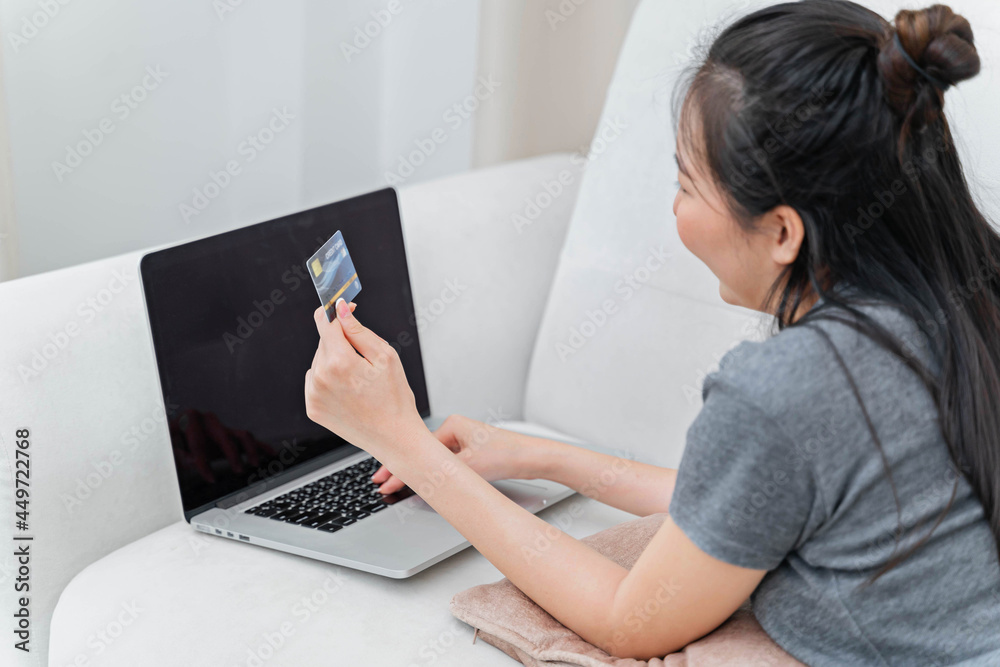 Asian woman using credit card for online payment with laptop while sitting at the living room. online shopping Pay by credit card via electronic wallet. Asian woman using credit card for online payment with laptop while sitting at the living room. online shopping Pay by credit card via electronic wallet.