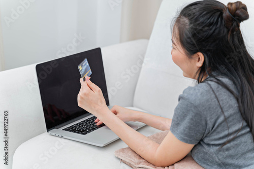 Asian woman using credit card for online payment with laptop while sitting at the living room. online shopping Pay by credit card via electronic wallet.