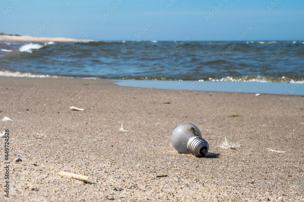 Obraz premium Garbage on the beach. A glass bulb on the seashore. Pollution of the coast.