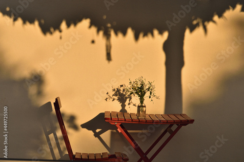 Red table and chair in the patio illuminated by the evening light and the shadow of a tree