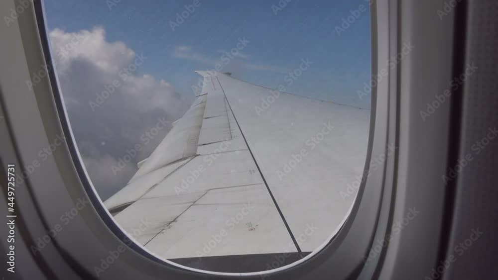 Airplane window with wing and cloudy sky behind.