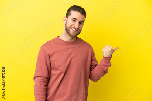 Handsome blonde man over isolated yellow background pointing to the side to present a product