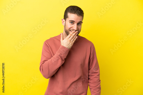 Handsome blonde man over isolated yellow background happy and smiling covering mouth with hand