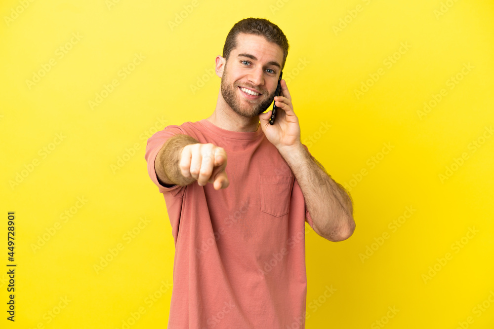 Handsome blonde man using mobile phone over isolated background pointing front with happy expression