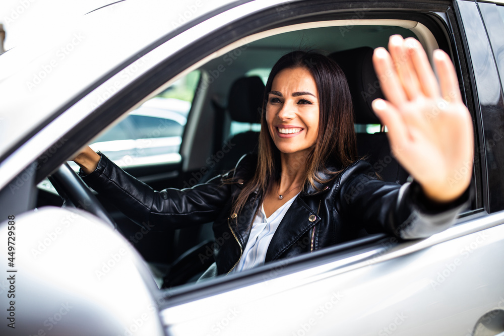 Young smiling woman greeting with hand from car. Cheerful caucasian girl welcome somebody sitting in automobile