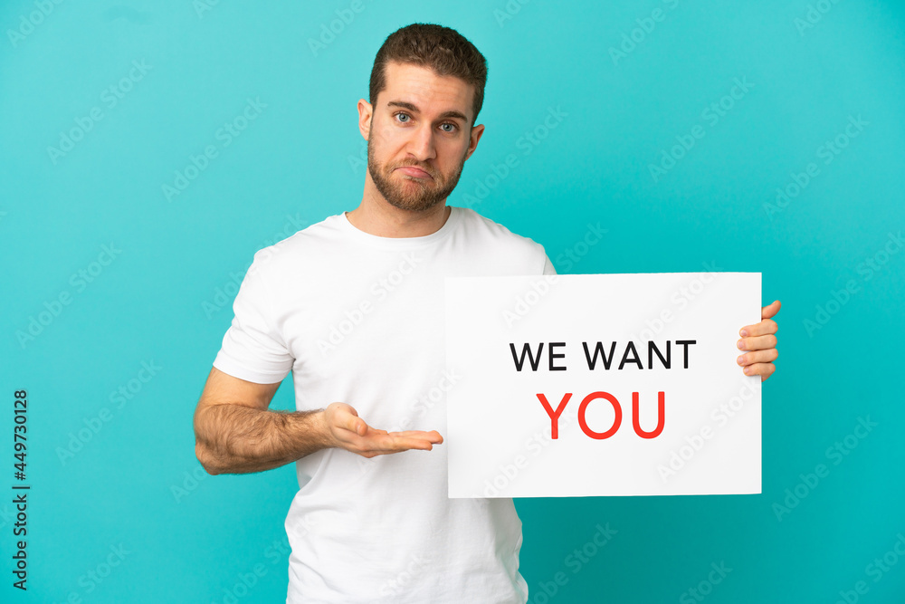 Handsome blonde man over isolated blue background holding We Want You board and pointing it Handsome blonde man over isolated blue background holding We Want You board and pointing it