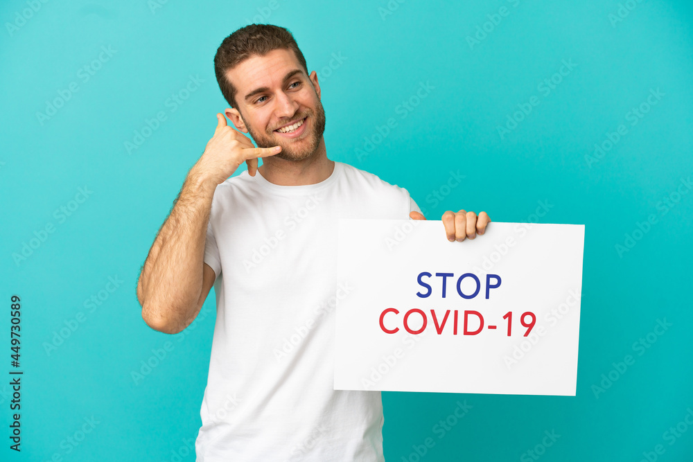 Handsome blonde man over isolated blue background holding a placard with text Stop Covid 19 and doing phone gesture Handsome blonde man over isolated blue background holding a placard with text Stop Covid 19 and doing phone gesture