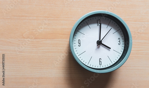 Round shaped analog clock, gray on a wooden table.