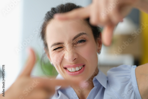 Young woman winks and makes a gesture with hands to photo frame