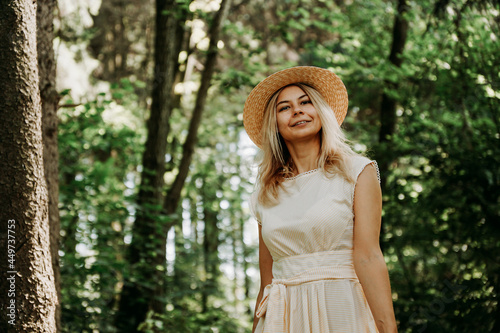 Beautiful young woman in a straw hat and white dress in a green park or forest on a summer day