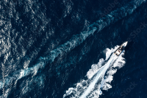 View from above, stunning aerial view of a boat cruising on a blue water creating a wake. Costa Smeralda, Sardinia, Italy. © Travel Wild