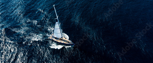 View from above, stunning aerial view of a sailboat sailing on a blue water at sunset. Costa Smeralda, Sardinia, Italy.