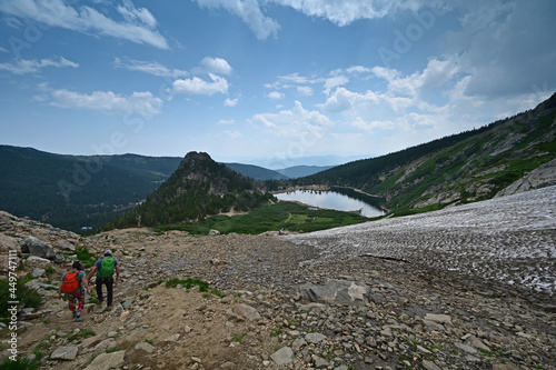 Hikers descend Saint Mary's Glacier Trail in Arapaho National Forest, Colorado on sunny summer afternoon with St Mary's Lake in background.