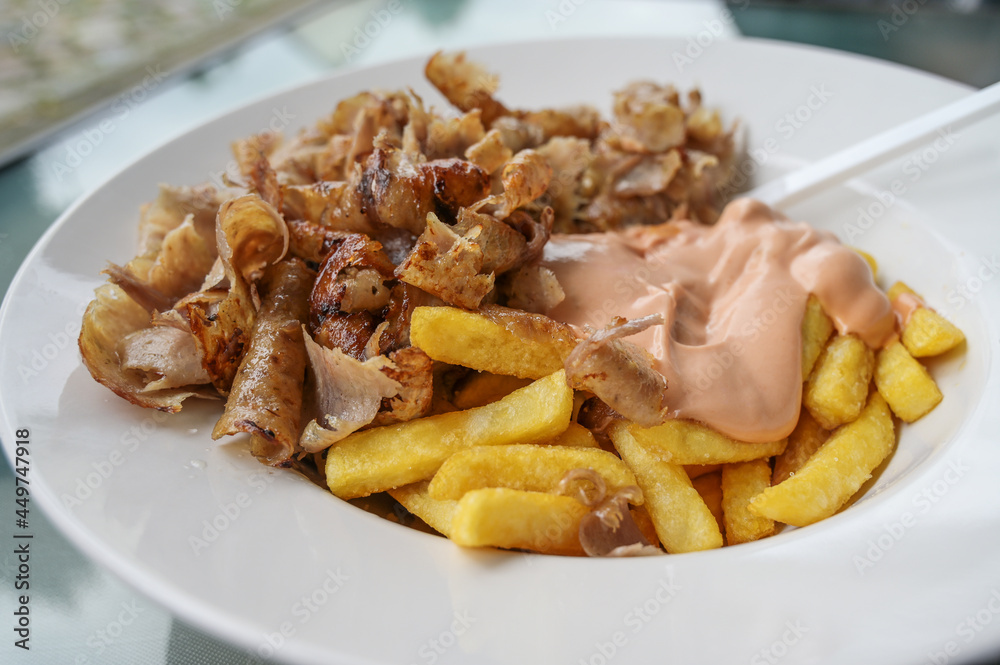 Doner kebab meat from a turkish rotating spit with french fries and cocktail sauce on a white plate in a fast food restaurant, selected focus