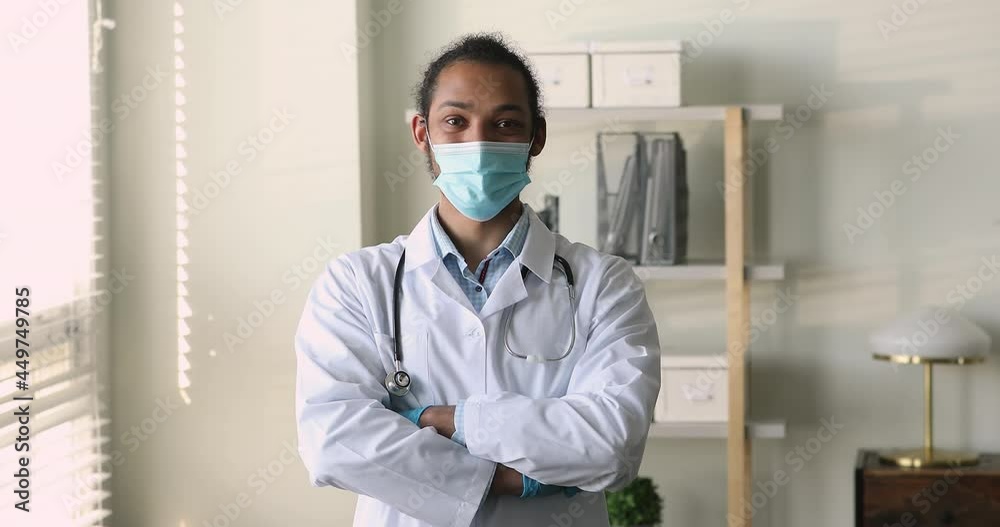 Young African therapist wear mask protective gloves uniform stethoscope on neck standing at workplace in clinic office with arms crossed looks into distance, professional aid, doctor portrait concept Young African therapist wear mask protective gloves uniform stethoscope on neck standing at workplace in clinic office with arms crossed looks into distance, professional aid, doctor portrait concept