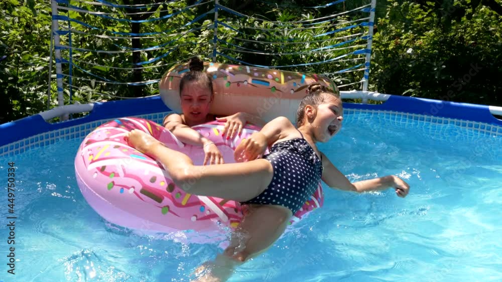 Girl throw down kid from donut float on sunny summer day, pool games