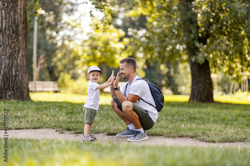 The family is having fun in the park. Father and son are playing in the forest dressed in the same casual summer clothes on a beautiful sunny day. Dad squats as the boy hi five to him. Making memories