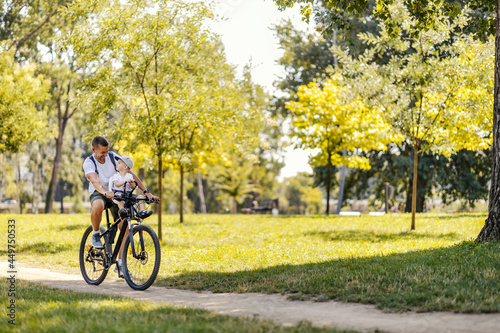 Father and son bonding time in nature. A little boy is sitting in a bicycle basket while his father rides a bicycle through the woods. Beautiful sunny day in nature to hanging out with family