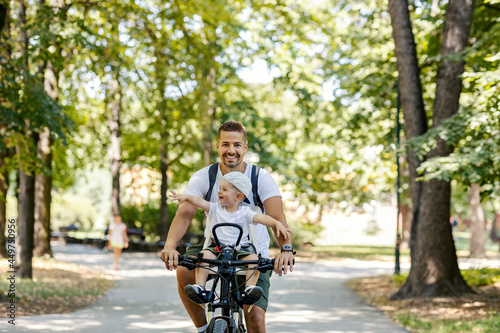 Weekend for family activities. The toddler boy is sitting in a bicycle basket while his father rides his bicycle through the woods. Father and son bonding, healthy lifestyle, goofing around