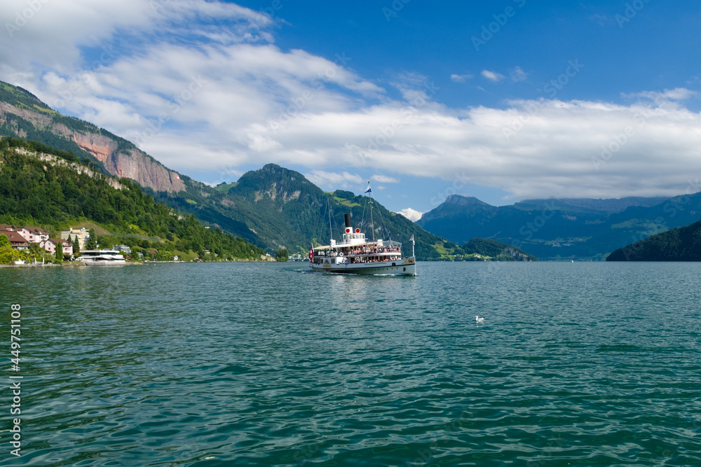 Sunny view of the old wheeled boat sailing near the village of Weggis facing the lake of Luzern with the Swiss mountains in the background