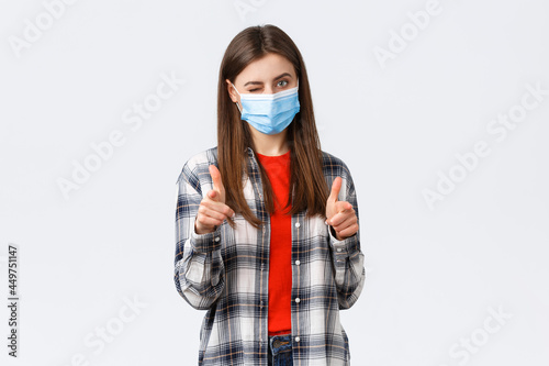 Coronavirus outbreak, leisure on quarantine, social distancing and emotions concept. You can dot it. Supportive young attractive female in medical mask pointing at camera, wink and congratulate photo