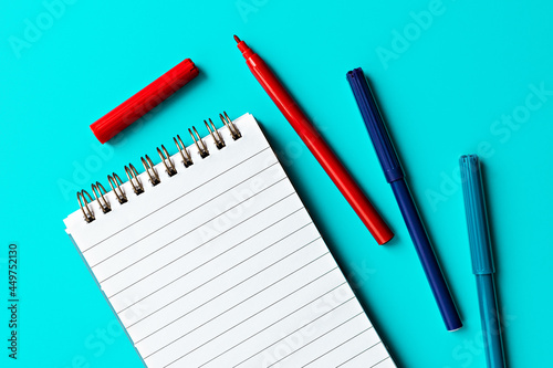 empty white notepad and multi-colored markers on turquoise background.  template for text and design